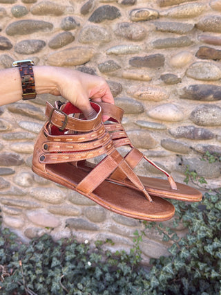 Brown sandal held by a hand against a stone wall background