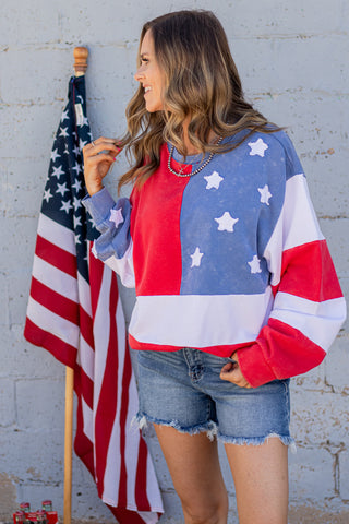 Woman wearing a colorful star-patterned sweatshirt standing next to an American flag.