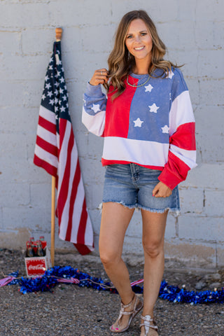 Woman wearing a colorful sweater with star pattern, standing in front of an American flag.