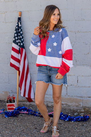 Woman wearing a colorful sweatshirt with star patterns, standing in front of an American flag.