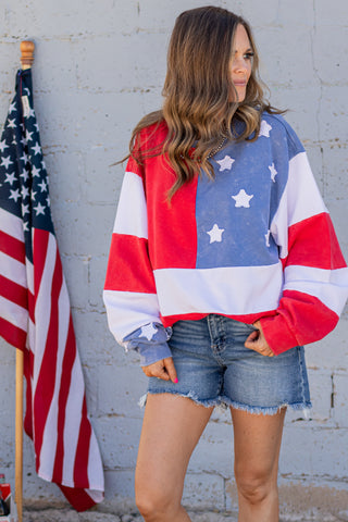 Person wearing a flag-themed sweatshirt with an American flag in the background