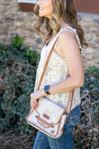 Woman holding a white handbag with brown accents outdoors