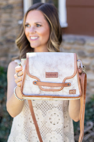 Woman holding a white handbag with brown accents outdoors