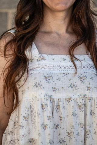 Close-up of a woman wearing a sleeveless cream-colored dress with a delicate blue and yellow floral print and lace trim.