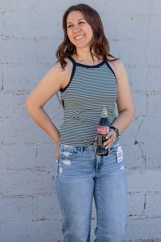 Woman wearing a striped tank top and jeans against a light gray wal