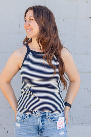 Woman wearing a striped tank top and jeans against a light gray wall