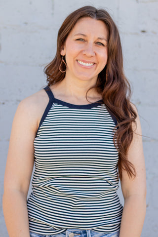 Woman wearing a striped tank top and jeans against a light gray wal