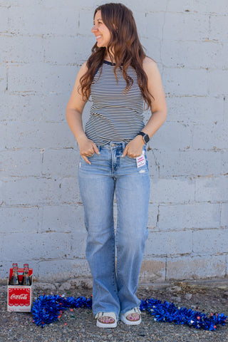 Woman wearing a striped tank top and jeans against a light gray wal