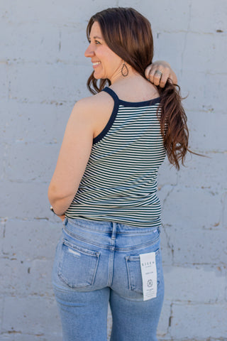 Woman wearing a striped tank top and jeans against a light gray wal