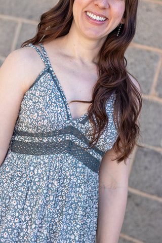 Woman wearing a green floral dress with lace details, smiling outdoors.