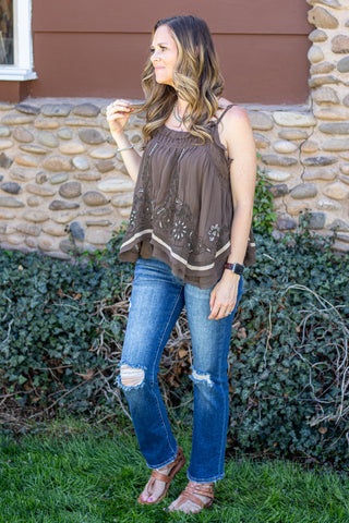 Woman wearing an olive embroidered tank top with blue jeans against a natural background