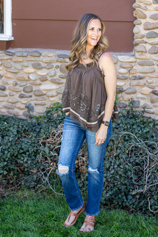 Woman wearing an olive embroidered tank top with blue jeans against a natural background