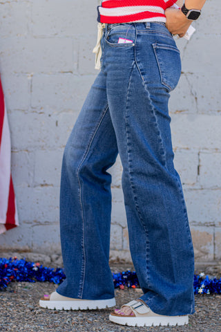 Person wearing blue jeans with a red and white striped shirt in front of a gray wall.