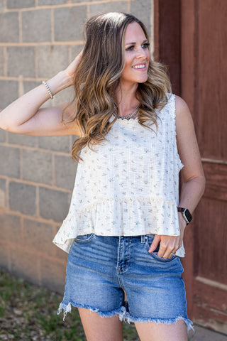 Woman wearing a white lace top and denim shorts standing against a brick wall.