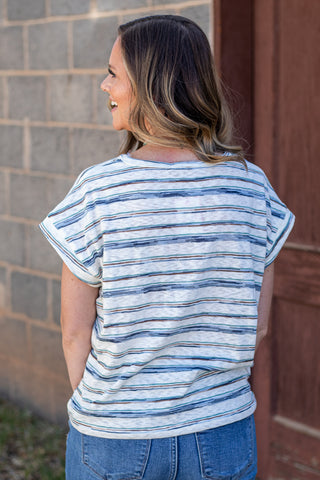 Woman wearing a striped shirt and jeans against a stone wall.