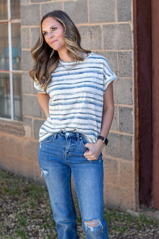 Woman wearing a striped shirt and jeans against a stone wall.