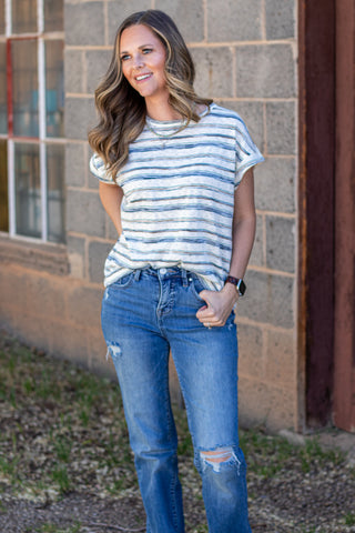Woman wearing a striped shirt and jeans against a stone wall.