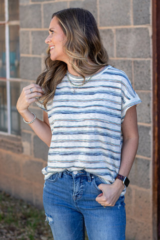 Woman wearing a striped shirt and jeans against a stone wall.
