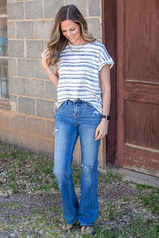 Woman wearing a striped shirt and jeans against a stone wall.