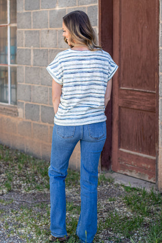 Woman wearing a striped shirt and jeans against a stone wall.