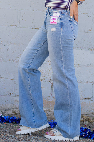 Person wearing light blue flared jeans with brand tags against a white brick wall.
