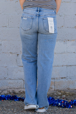 Person wearing blue jeans with a brand tag, standing against a gray wall with decorative blue elements on the ground.