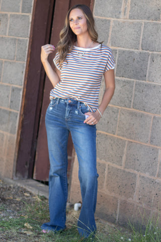 Woman wearing a blue, copper and white striped short sleeve top with a pair of dark wash denim. 