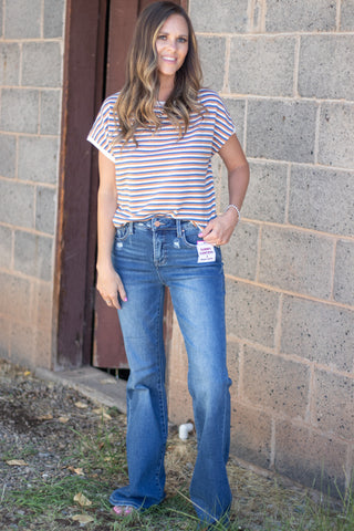 Woman wearing a blue, copper and white striped short sleeve top with a pair of dark wash denim. 