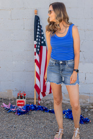 Woman wearing a blue striped tank top and denim shorts standing in front of an American flag.