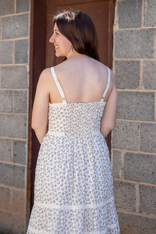 Woman wearing a white floral dress standing against a brick wall.