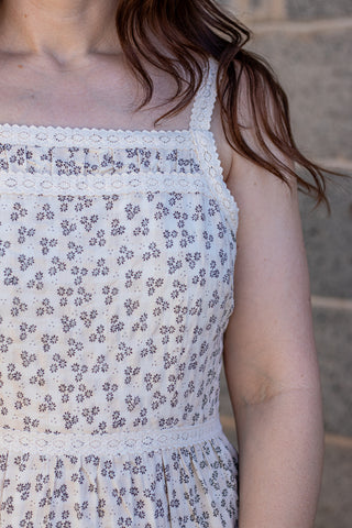 Woman wearing a white floral dress standing against a brick wall.