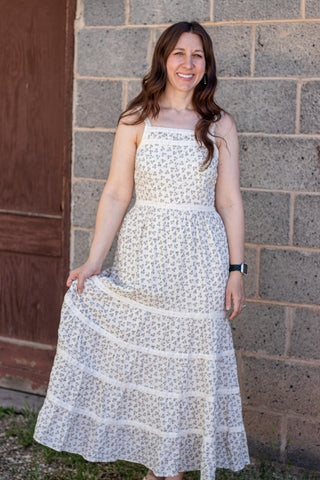 Woman wearing a white floral dress standing against a brick wall.