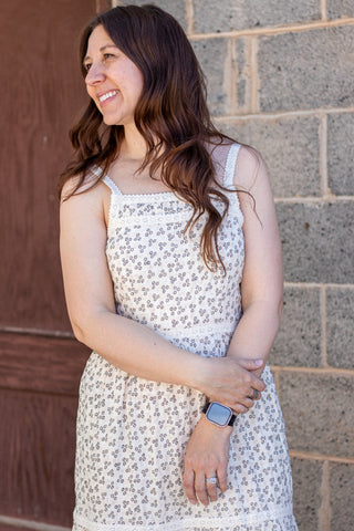 Woman wearing a white floral dress standing against a brick wall.