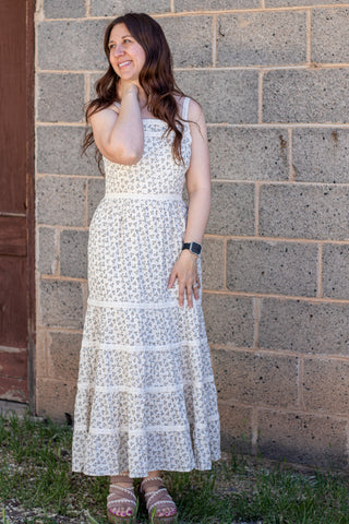 Woman wearing a white floral dress standing against a brick wall.