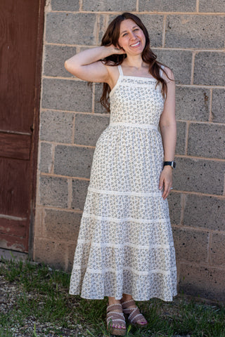 Woman wearing a white floral dress standing against a brick wall.