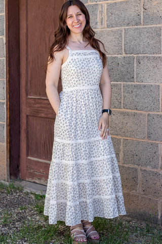 Woman wearing a white floral dress standing against a brick wall.