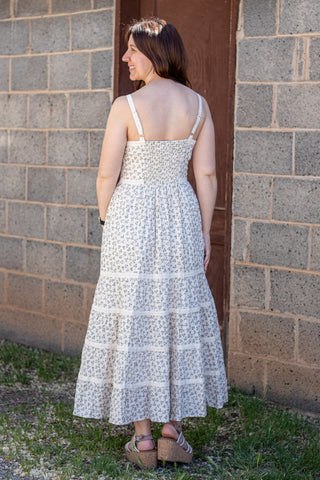 Woman wearing a white floral dress standing against a brick wall.
