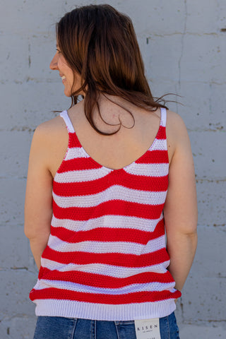 Woman wearing a tank top with an American flag design, standing next to a brick wall and American flag.