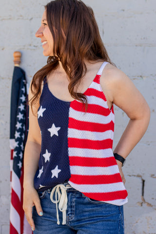 Woman wearing a tank top with an American flag design, standing against a textured wall.