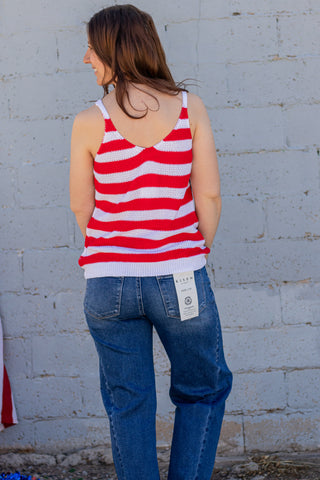Woman wearing a tank top with an American flag design, standing next to a brick wall and American flag.