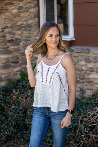 Woman wearing a white blouse with colorful  floral embroidery and blue jeans outdoors.